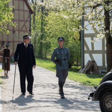 Szene aus dem Tatort, der im Hessenpark gedreht wurde. Sie zeigt Ulrich Tukur und Ludwig Simon wie sie durch die Baugruppe Mittelhessen laufen.