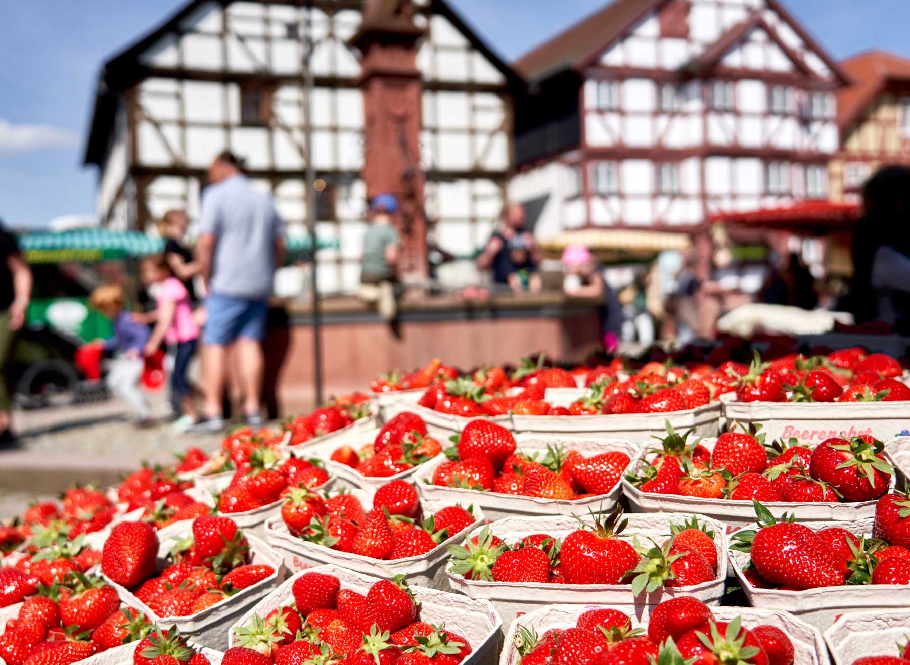 Marktstand mit frischen Erdbeeren vor dem Brunnen und einem Fachwerkhaus