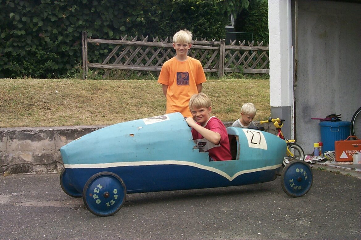 3 Kinder bereiten sich auf ein Seifenkistenrennen vor.