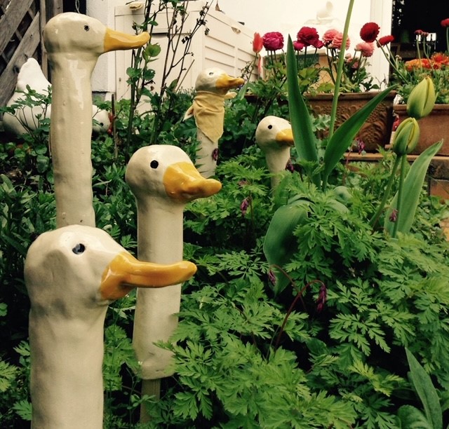 getöpferte Gänseköpfe in einem Blumenbeet